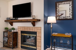 Living Area- This bright, open living room has a flat screen TV and a gas fireplace. - Photo of living room wall featuring a gas fireplace with wooden mantle and a flat screen smart TV above it.