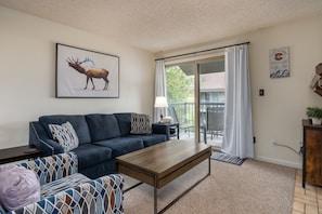 Living Area- Relax after a long day of recreating! - Blue couch, patterned arm chair, coffee table, painting of elk above couch, sliding glass door to porch.