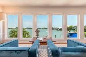 Enjoy breathtaking waterfront views from this cozy sitting area with plush seating and floor-to-ceiling windows, bringing in natural light and stunning Dauphin Island scenery.