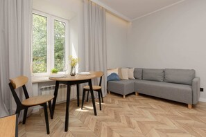 A spacious living room featuring a grey sofa, a dining table, and large windows overlooking greenery.
