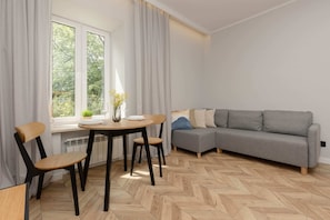 A spacious living room featuring a grey sofa, a dining table, and large windows overlooking greenery.
