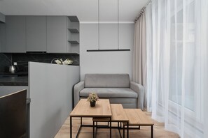 Compact living area with a dining table, sofa, and bright natural lighting from the windows.