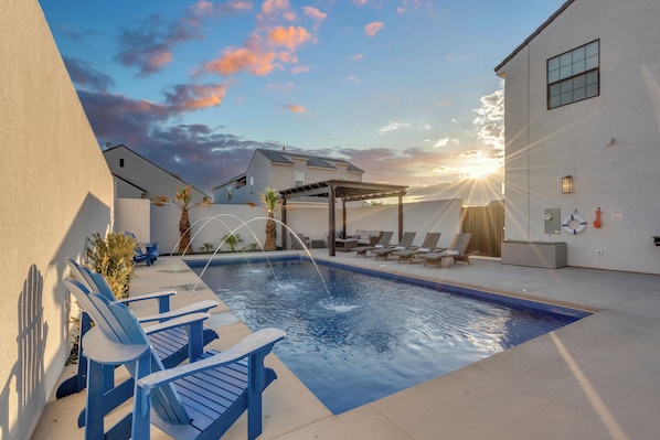 Relax in this modern private retreat featuring a sparkling pool, cozy lounge chairs, and a stunning sunset view.
