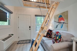 Charming living space with loft bedroom access, comfortable seating, and a wall-mounted TV | features natural light, modern amenities, and a fully equipped kitchenette ideal for a relaxing and convenient stay.