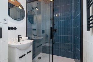 The bathroom featuring modern decor with blue tiles, a shower with a glass panel, a white sink, and minimalistic fixtures.