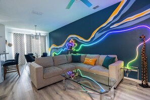 Open concept living area with plush sectional and exciting neon wall art