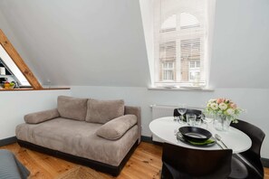 A living area with a comfortable grey armchair, a small wooden coffee table, and a decorative flower arrangement.
