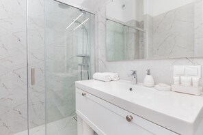 A sleek bathroom with a walk-in shower, white vanity, and marble-style tiles for a luxurious touch.
