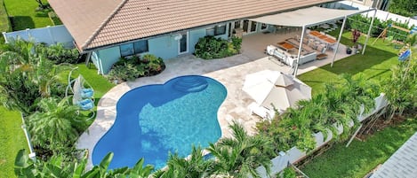 Resort style back yard with heated pool, shaded sofa seating and dining, BBQ grill, sun loungers and children's swing set