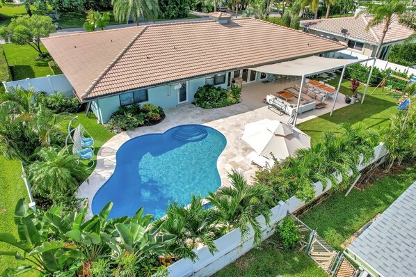 Resort style back yard with heated pool, shaded sofa seating and dining, BBQ grill, sun loungers and children's swing set