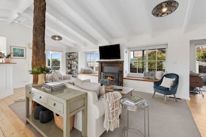 Under high ceilings, the heart of the home features a cosy wood-burning fireplace and plush linen lounges
