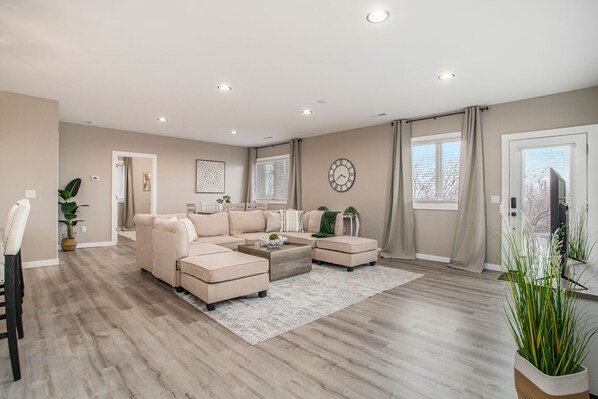 This beachy living room features a spacious light-colored sectional, perfect for lounging. The room is accented with lush greens, bringing the outdoors inside. 