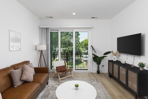 Cozy living room with a large, comfortable leather couch, Smart TV with all the streaming apps, and a balcony to let in the fresh air and natural light.