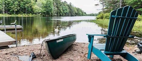 Relax by the water at Sunset Chalet. With a canoe ready for adventure and a chair just waiting for you, enjoy the perfect spot to unwind and take in the serene views of the lake and surrounding nature.