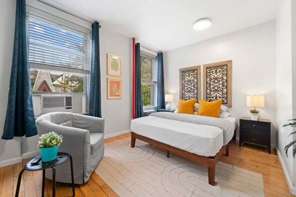 This is the primary bedroom featuring a comfortable queen-sized bed and two large windows, creating a bright atmosphere.