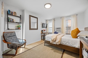 Spacious studio with large windows, a double bed, and a cozy spot to unwind
