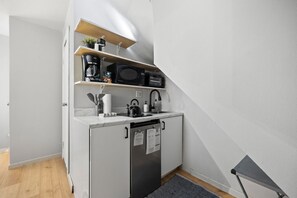 Compact kitchen with white cabinetry, a sink, microwave, toaster, coffee maker, and small plants for decoration.