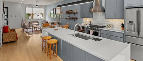 Modern open-concept kitchen and living area with soft blue cabinets, a sleek island, and warm natural wood flooring.