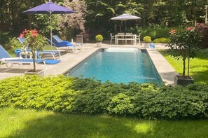 Backyard pool area has 4 lounge chairs and dining table for eating.