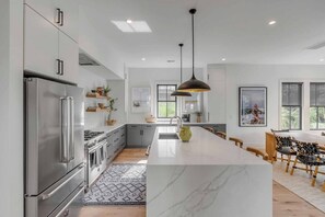 Modern Chef's kitchen with hardwood floors, high ceilings, stainless steel appliances, a dishwasher, pendant lighting, and a large island for food prep and seating.