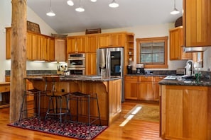 The fully equipped kitchen features high-end appliances, a large kitchen island with three barstools, ample cabinet and counter space, and classic wood finishes.