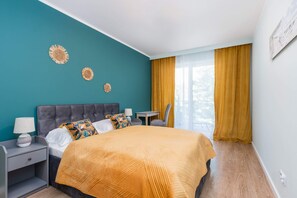 A cozy bedroom with a teal accent wall, a double bed covered with orange bedding, and decorative elements like golden wall hangings.