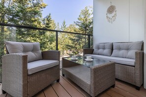 An outdoor seating area on a balcony, furnished with comfortable gray chairs and a table, surrounded by trees for a serene view.