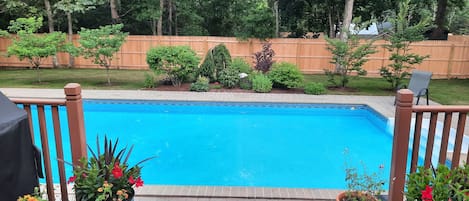 backyard deck with solar heated pool in fenced in yard