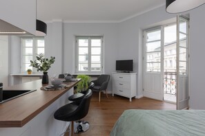 The studio features a comfortable double bed with mint-green bedding, positioned near large windows that fill the room with natural light.