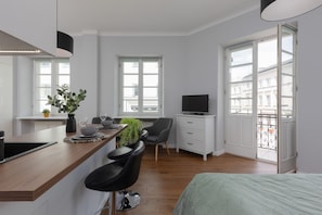 The studio features a comfortable double bed with mint-green bedding, positioned near large windows that fill the room with natural light.