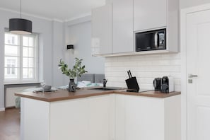 A compact and elegant kitchen in white tones is equipped with sleek modern appliances and minimalistic decor for a clean, functional look.