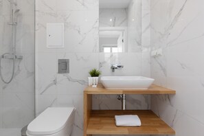 The marble-tiled bathroom exudes luxury with its walk-in shower, wooden vanity, and contemporary fixtures.