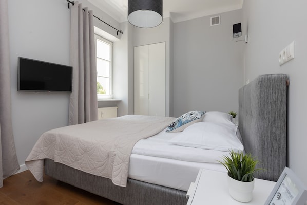 A cozy and modern studio with a double bed, a gray upholstered headboard, and neutral decor that creates a welcoming atmosphere.