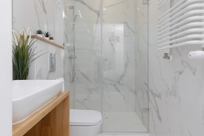 A clean and sleek bathroom with white marble-style tiles, a walk-in shower, and contemporary fixtures.