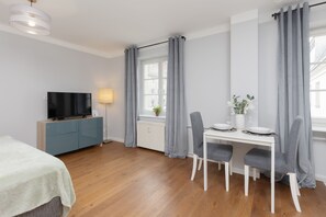 A bright and modern open-plan space with a double bed, a cozy sofa, and a wall-mounted TV, creating a comfortable multifunctional area.