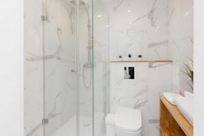  A luxurious bathroom with marble-style tiles, a glass-enclosed shower, and minimalist decor.