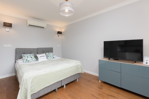 A bright and modern open-plan space with a double bed, a cozy sofa, and a wall-mounted TV, creating a comfortable multifunctional area.