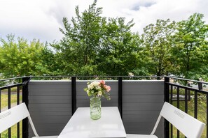 A charming balcony with a table and chairs, surrounded by lush green trees.

