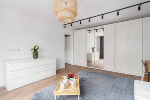 A view of the main living space featuring wood flooring, white furniture, and natural lighting.

