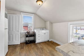 Small kitchen features an antique farmhouse sink, compact gas stove, toaster, drip coffee maker, fridge, freezer, microwave, pots, pans, and cookware. 