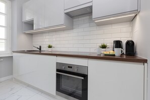 A clean and fully-equipped kitchen area featuring white cabinetry, a tiled backsplash, and wooden countertops.