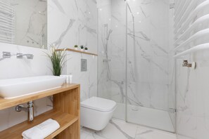 A modern bathroom with sleek white marble tiles, a walk-in shower, and minimalistic fixtures.
