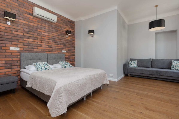 A bright and stylish living and sleeping area with a comfortable double bed, exposed brick wall, and modern furniture.