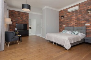 A bright and stylish living and sleeping area with a comfortable double bed, exposed brick wall, and modern furniture.