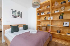 A neatly organized bed with soft bedding and vibrant purple accents, located in the same open-plan space.