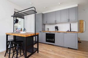 A fully equipped kitchen with gray cabinetry, a wooden countertop, and a small dining table with stylish barstools.
