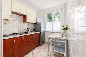 A fully equipped kitchen with wooden cabinets, tiled backsplash, and a dining table for two.