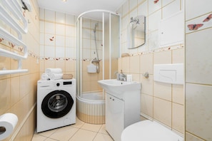 A compact bathroom with a washing machine, a shower cabin, and tiled walls for a functional layout.