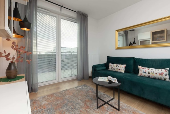 A stylish living room with a green sofa, coffee table, and large windows providing natural light.