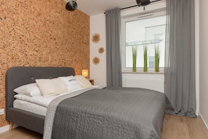 A cozy bedroom with a double bed, gray bedding, and a decorative cork feature wall.
